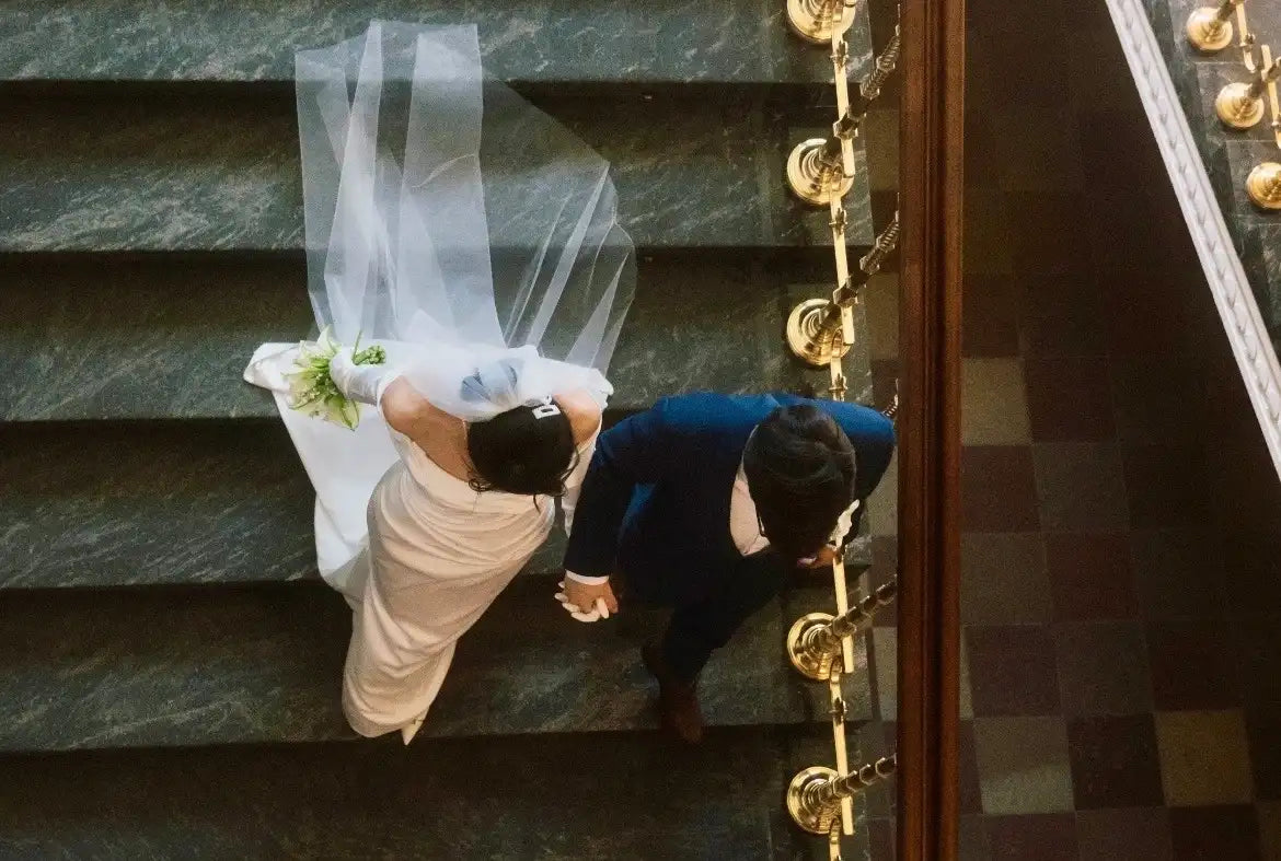 Jeunes mariés descendant des escaliers vus de haut, mettant en valeur le voile court de la tenue de mariage