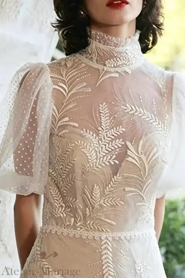 Détail du travail artisanal des broderies sur le bustier et le col montant, créant un décolleté cœur en transparence raffinée.