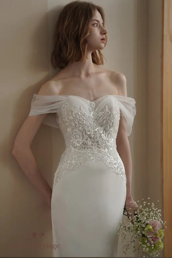 Structure corsetée d'une robe de mariée avec motifs floraux perlés et col Bardot romantique.