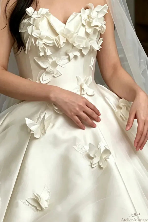 Détail des ailes de papillons en dentelle pailletée brodées sur la jupe volumineuse d'une robe de princesse.