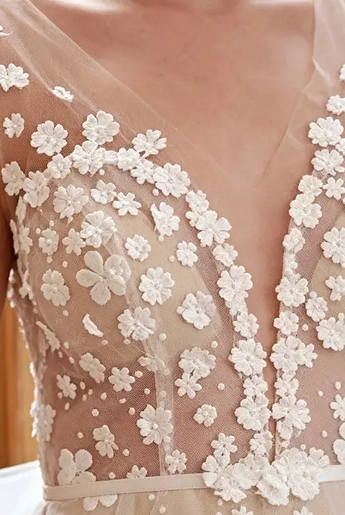 Détail des fleurs 3D brodées à la main sur le décolleté plongeant en V d'une robe de mariée bohème chic.