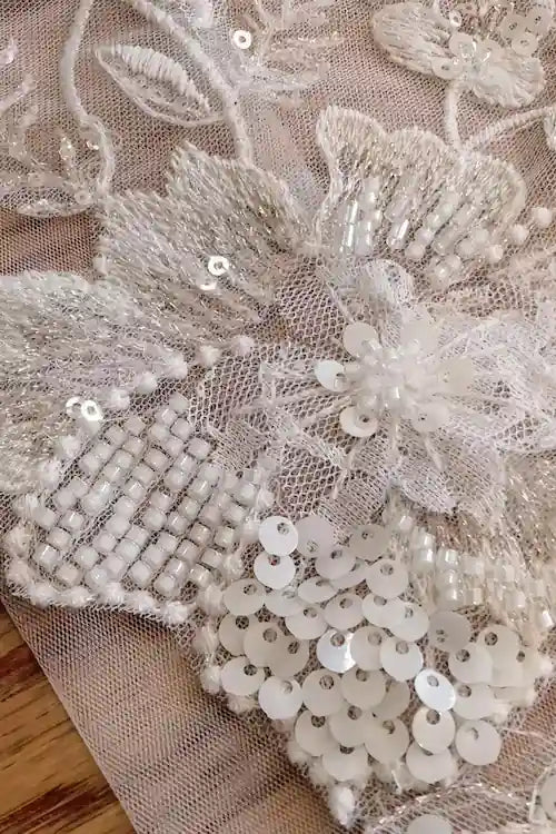 Gros plan extrême sur les détails de perlage et les sequins de haute couture brodés sur le tulle transparent des manches amovibles.