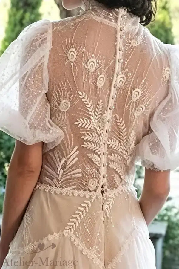 Vue détaillée du dos majestueux orné de motifs paon brodés et des manches bouffantes en tulle plumetis pour une mariée bohème chic.