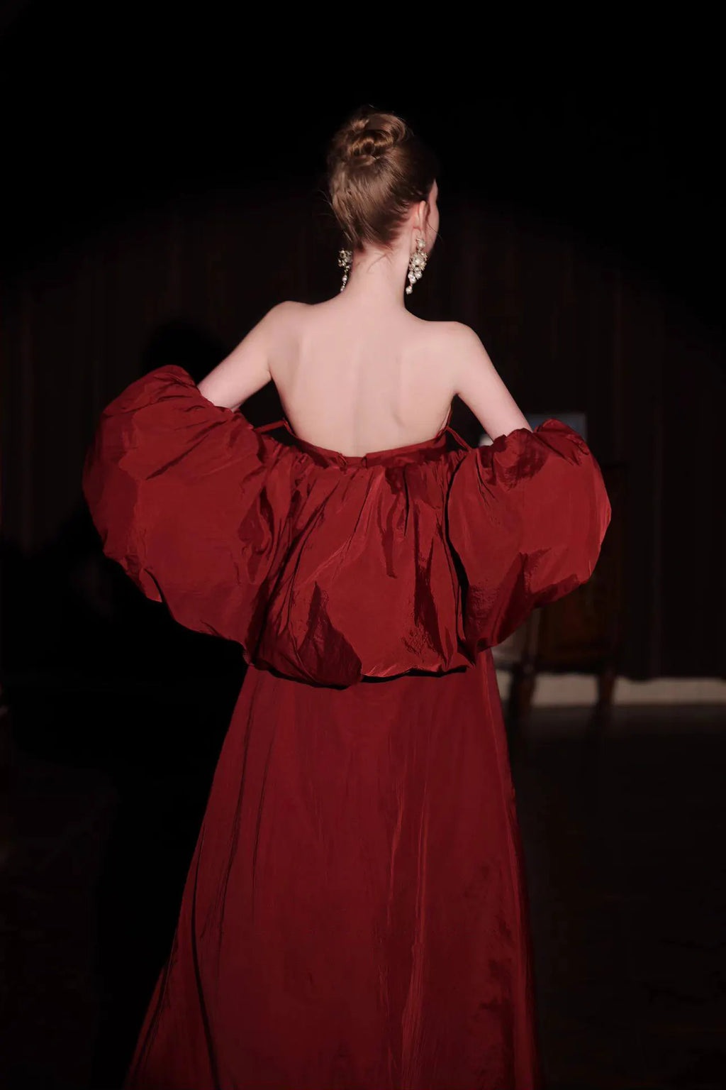 Vue de dos d'une robe haute couture rouge bordeaux mettant en valeur le dos nu et le volume dramatique des manches en taffetas.