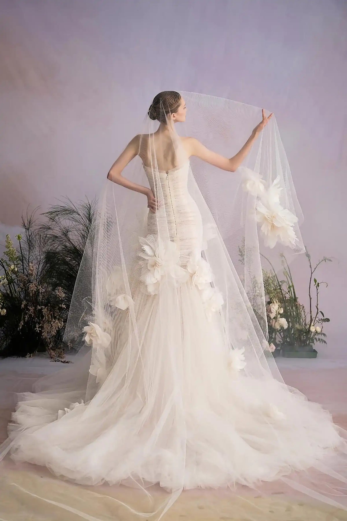 Vue de dos d'une robe de mariée coupe sirène avec une longue traîne fluide et un voile romantique.