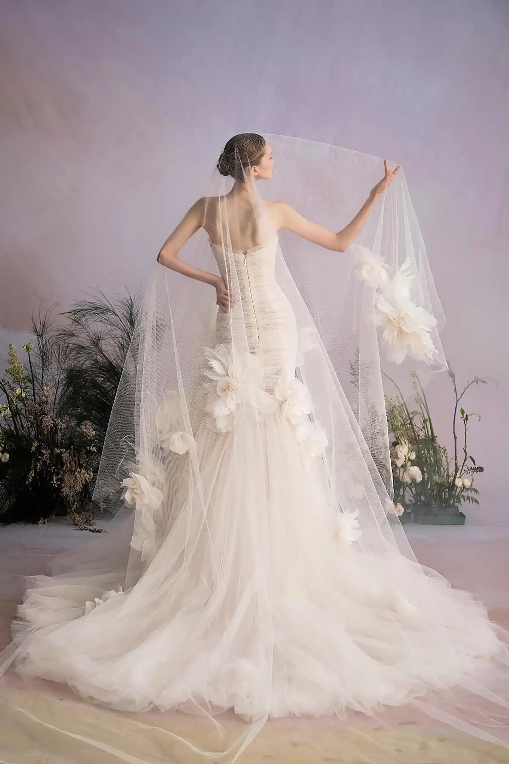 Vue de dos d'une robe de mariée coupe sirène avec une longue traîne fluide et un voile romantique.