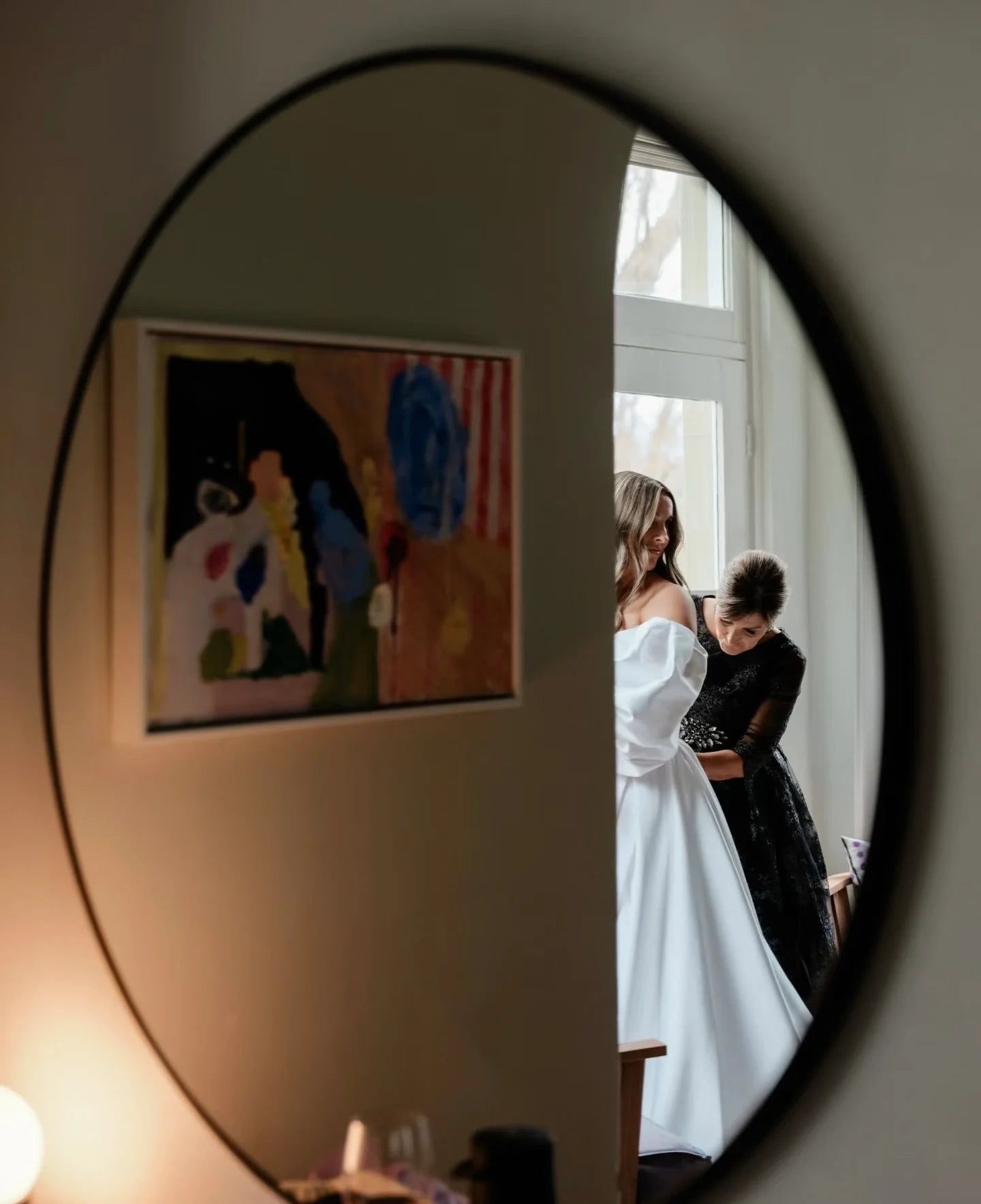 Ajustement sur-mesure d'une robe de mariée en atelier, vue à travers un miroir rond pour sublimer la morphologie