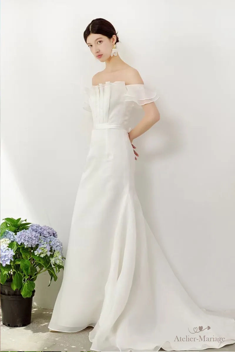 Femme en robe de mariée chic et simple bohème debout, mains derrière le dos