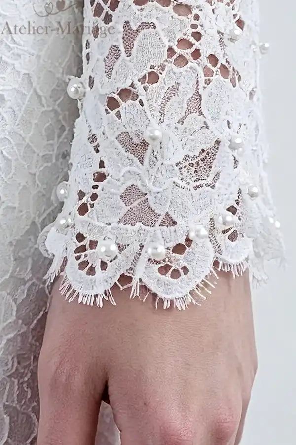Zoom sur le poignet boutonné avec perles et la dentelle fine, témoignant d'une confection artisanale française.