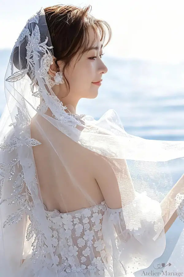 Portrait d'une mariée portant le col bardot orné de fleurs 3D avec un voile en dentelle assorti, capturant une ambiance féerique au bord de l'eau.