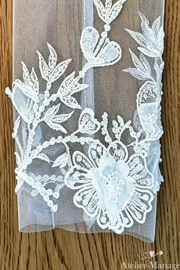 Manche amovible en dentelle artisanale et perles posée à plat montrant les détails de broderie