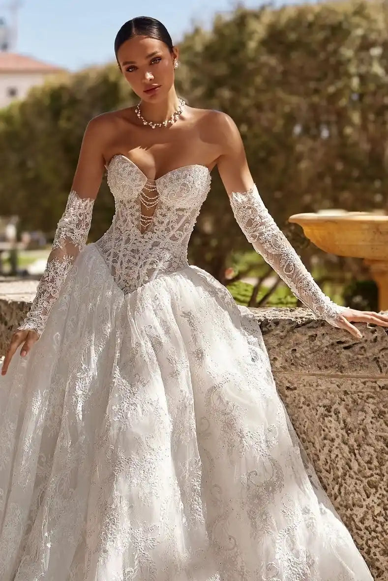 Look de mariage chic et romantique avec une mariée posant près d'une fontaine, sublimée par ses manches amovibles en dentelle fine.