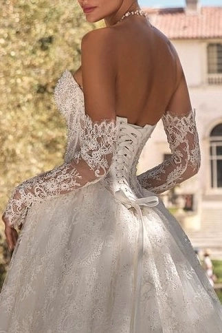 Vue de dos d'une mariée en robe à laçage corset, dévoilant l'intégration harmonieuse des manches amovibles en dentelle sur les bras.
