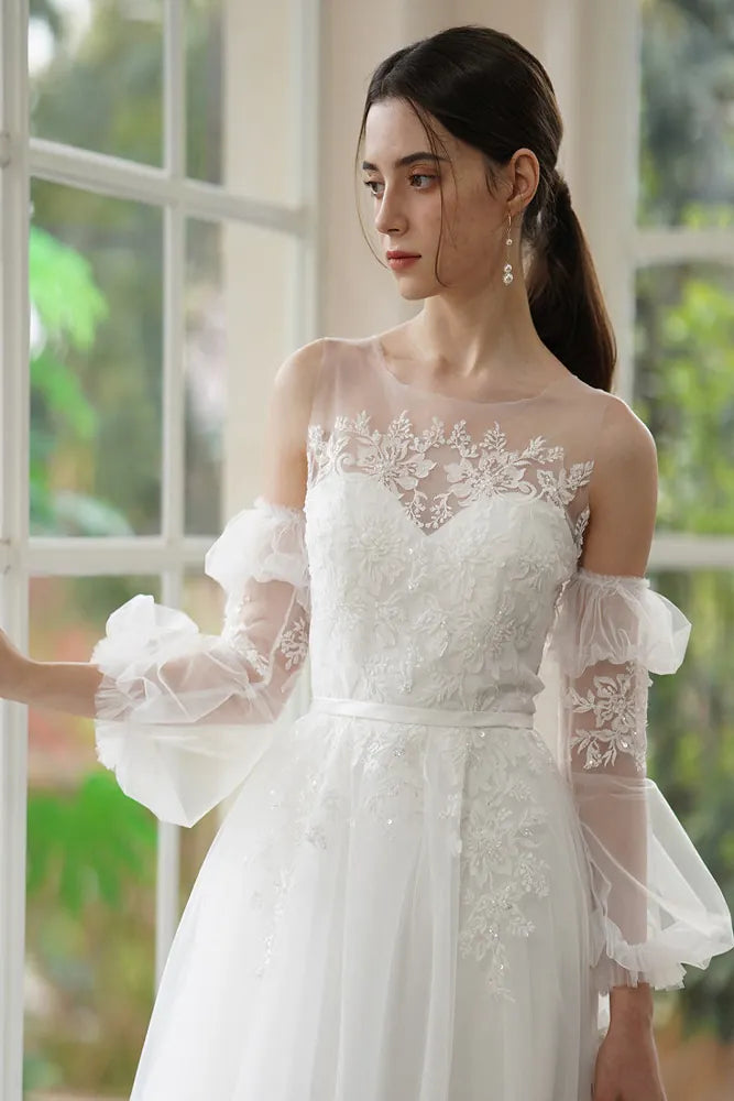 Mariée portant des manches amovibles en double tulle forme lanterne, ornées de fleurs 3D et perles discrètes.