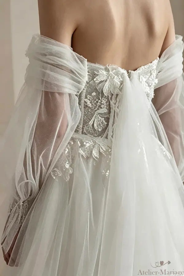 Fusion invisible entre les manches évasées et le col bardot d'une robe de mariée.