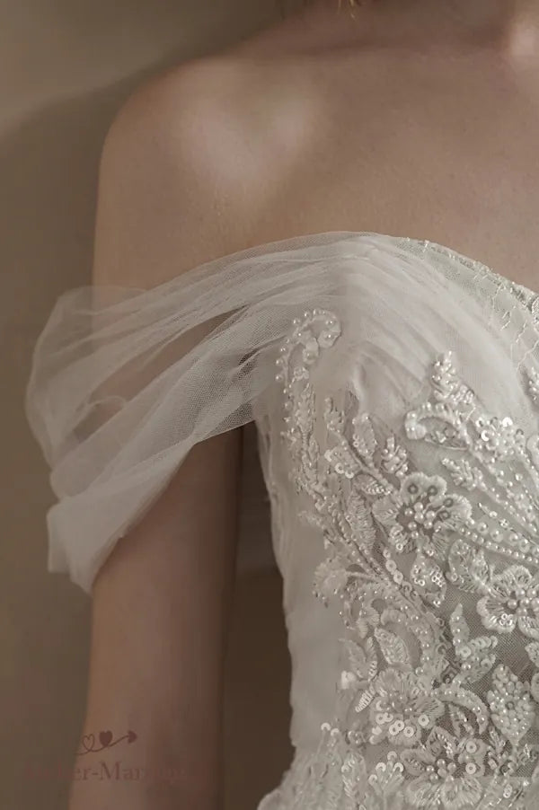 Mise en valeur du port de tête avec un décolleté Bardot perlé et des micro-manches en tulle.