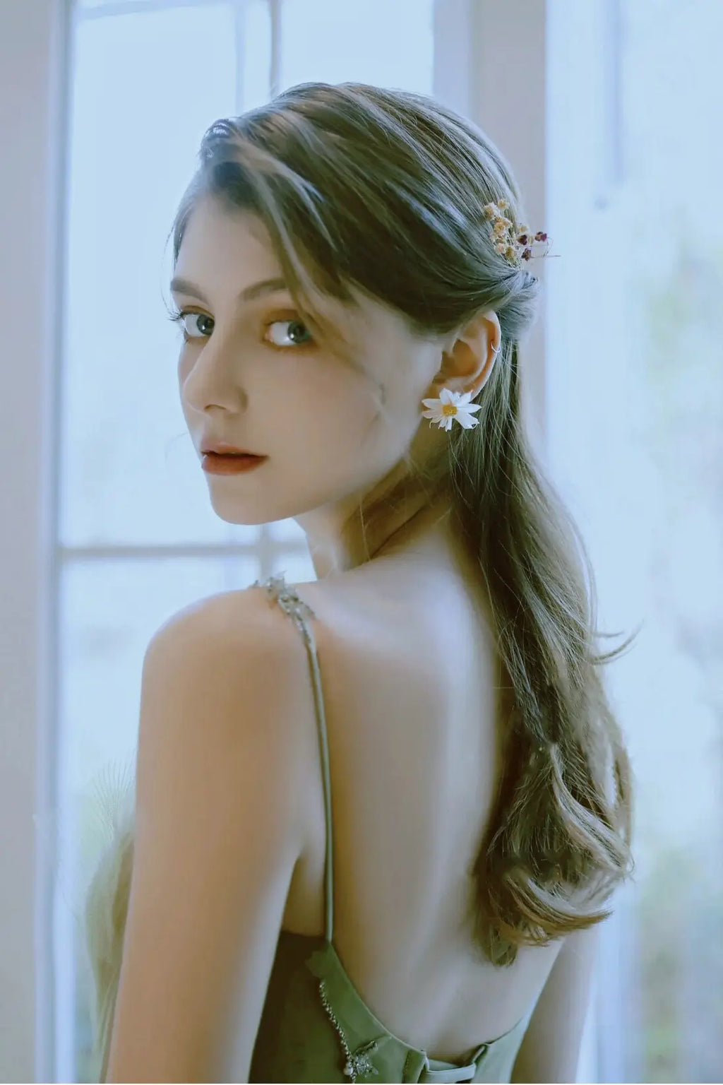 Portrait romantique d'une mariée regardant par-dessus son épaule, dévoilant les fines bretelles et le dos nu de sa robe vert sauge.