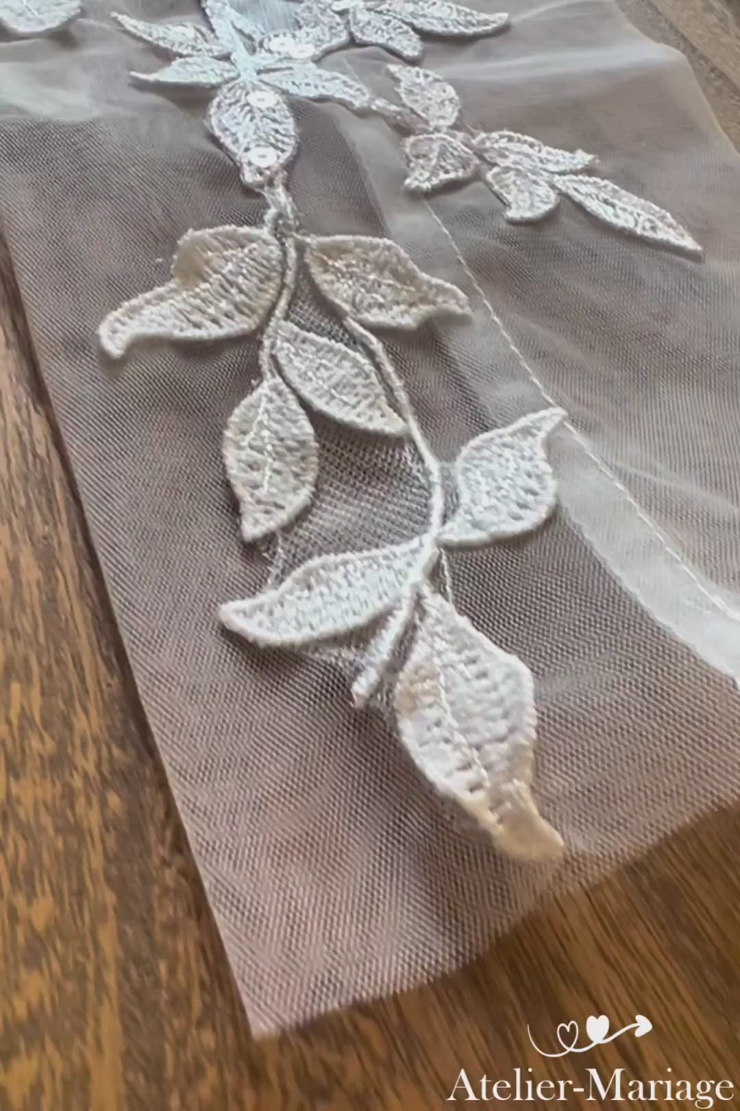 Vidéo des manches amovibles mariage en dentelle — shooting du poignet jusqu'aux fleurs satin 3D, finitions artisanale sur plateau bois