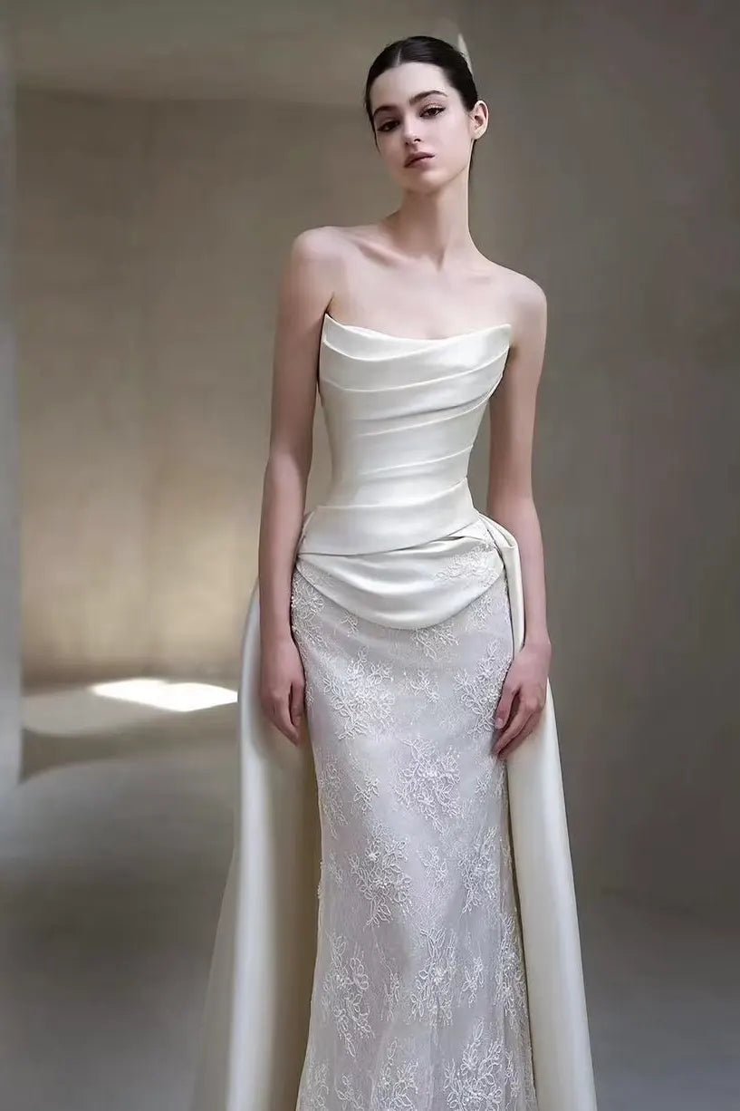 Mariée de face portant une robe sirène haute couture avec un bustier drapé en satin et une jupe en dentelle fine.