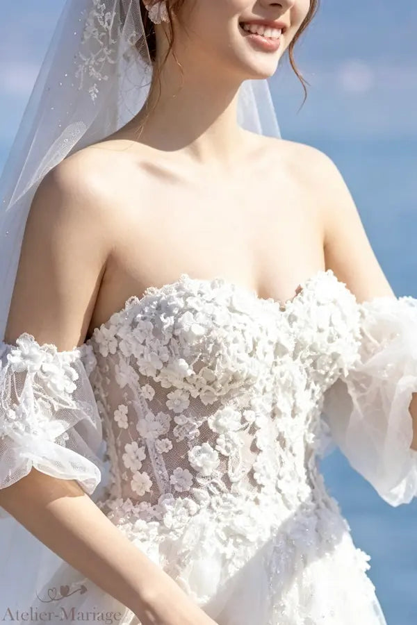 Vue rapprochée du bustier col bardot avec ses fleurs 3D en relief, montrant le rendu naturel et romantique lors d'un essayage réel.