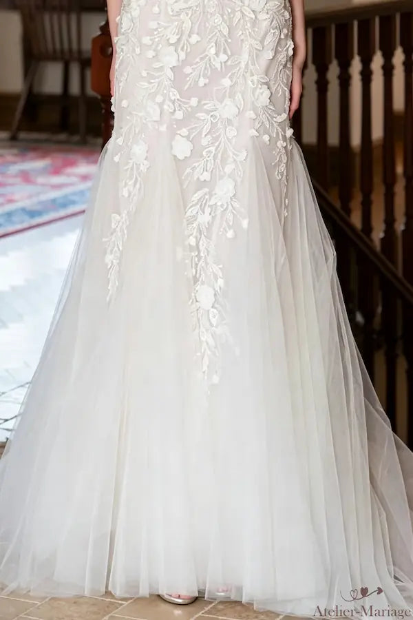 Gros plan sur la traîne en tulle léger et vaporeux, soulignant la délicatesse des applications de dentelle et l'ampleur gracieuse de la jupe. Commandez dès maintenant votre robe sur mesure.