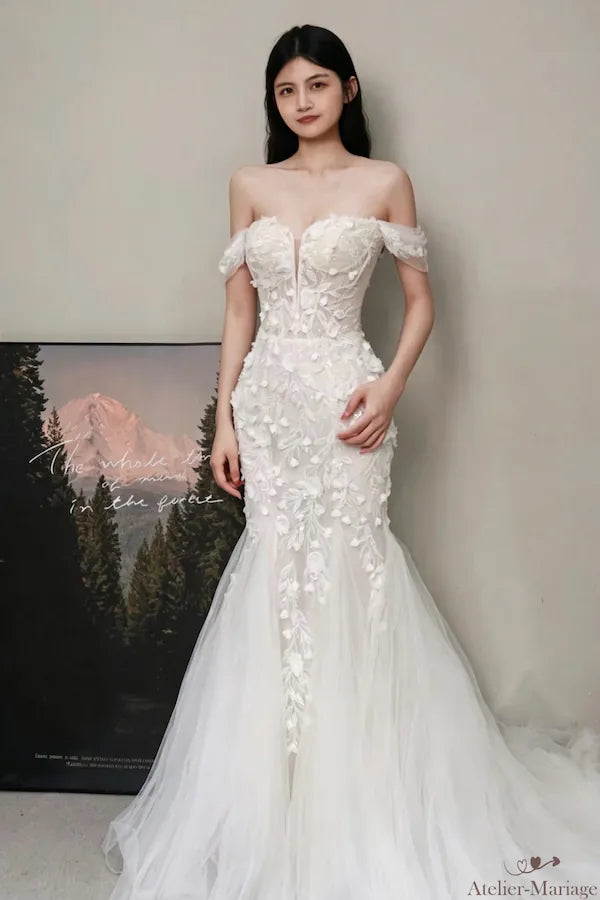 Nouvelle vue complète de la mariée portant la robe, avec une pose différente des mains croisées. Met en valeur l'harmonie du design et la coupe impeccable.