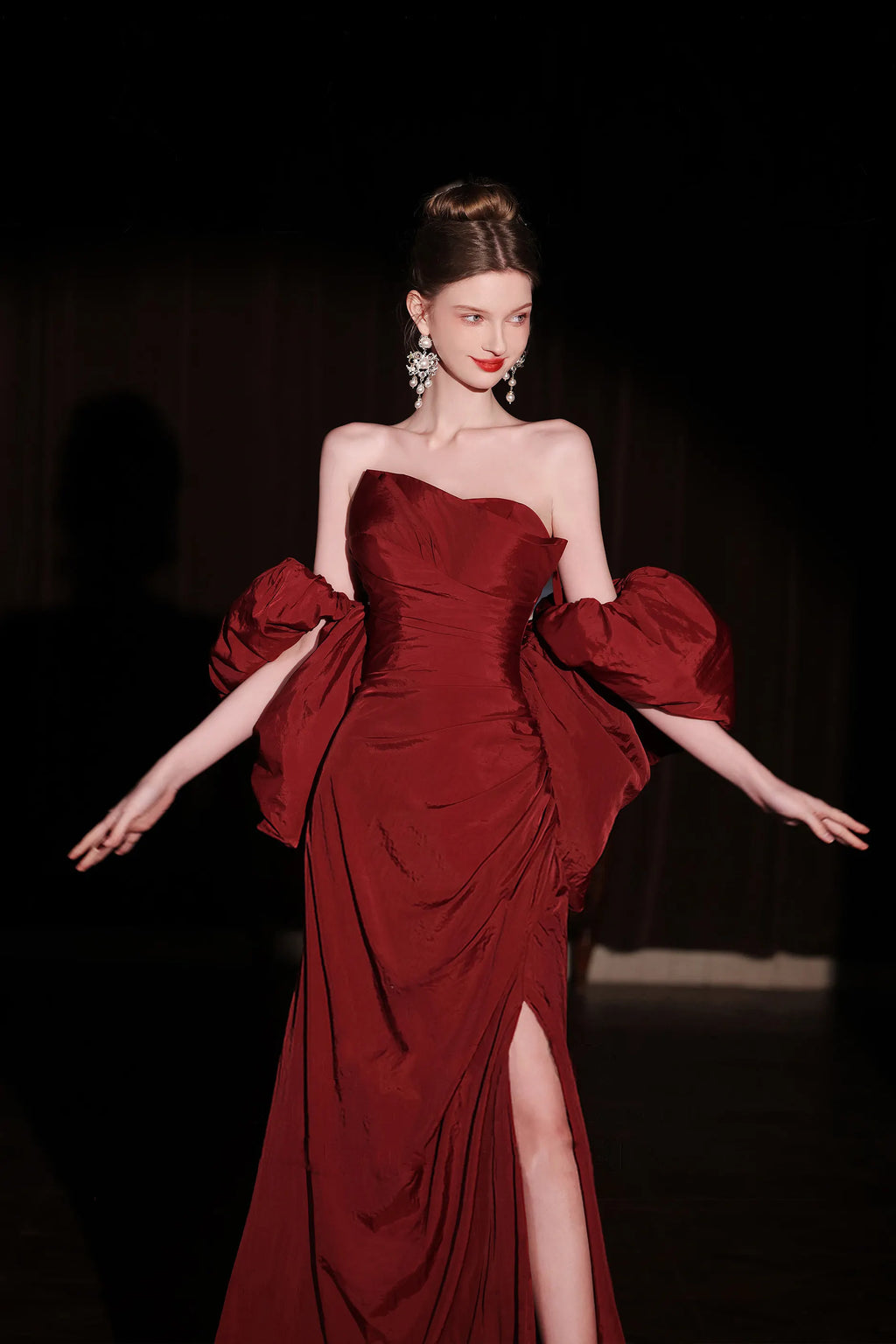 Mannequin posant avec une robe rouge bordeaux glamour fendue sur la jambe, idéale pour un mariage original ou un gala.