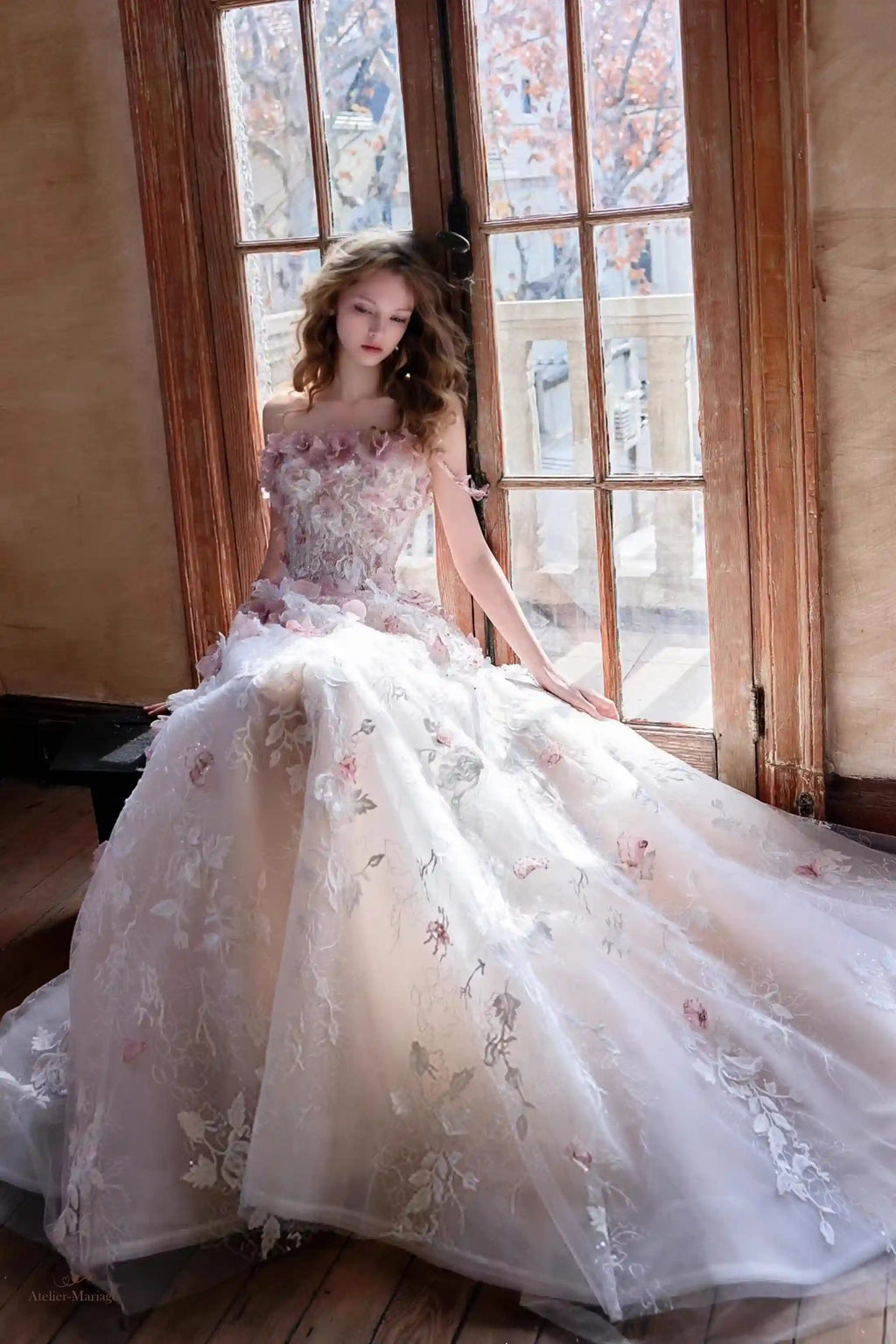 Femme assise portant une robe de mariée ou de gala féerique en tulle blush avec fleurs en relief.