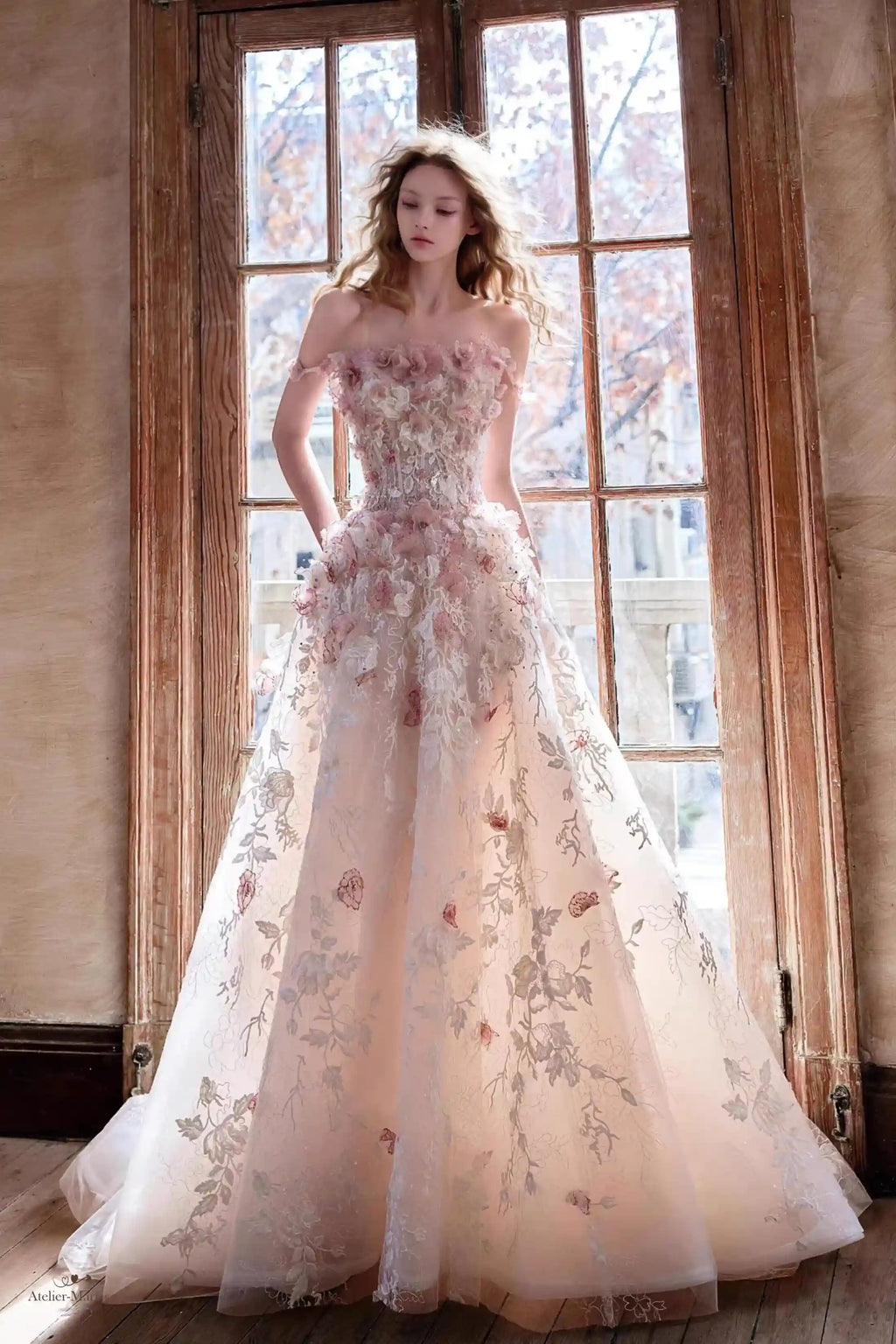 Mariée portant une robe blush romantique ornée de fleurs 3D et broderies argentées.