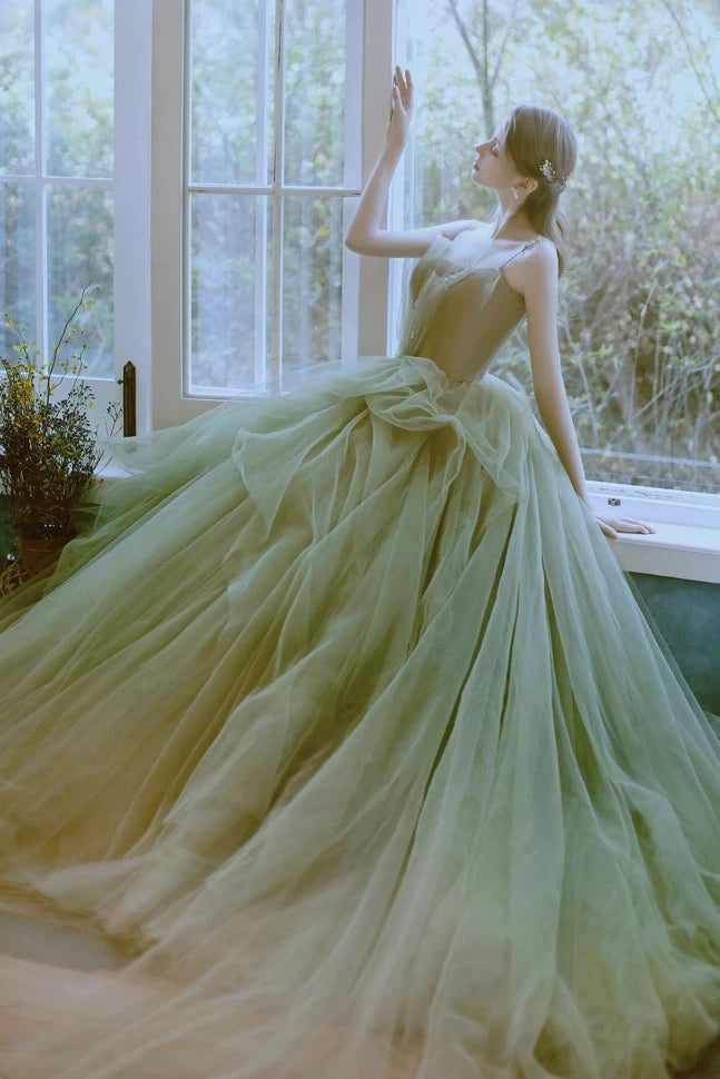 Mariée assise près d'une fenêtre portant une robe romantique vert olive en tulle superposé.