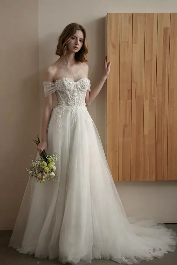 Robe de mariée avec col bardot et dos nu, ornée de fleurs 3D artisanales.