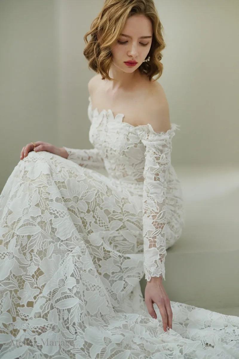Mariée portant une robe en dentelle à manches longues col Bardot, assise