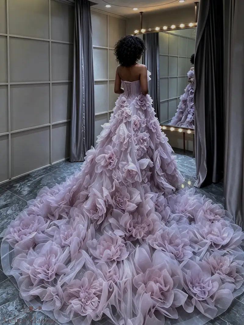 Mariée à la peau mate de dos, portant une robe princesse lilas spectaculaire avec traîne en fleurs 3D XXL