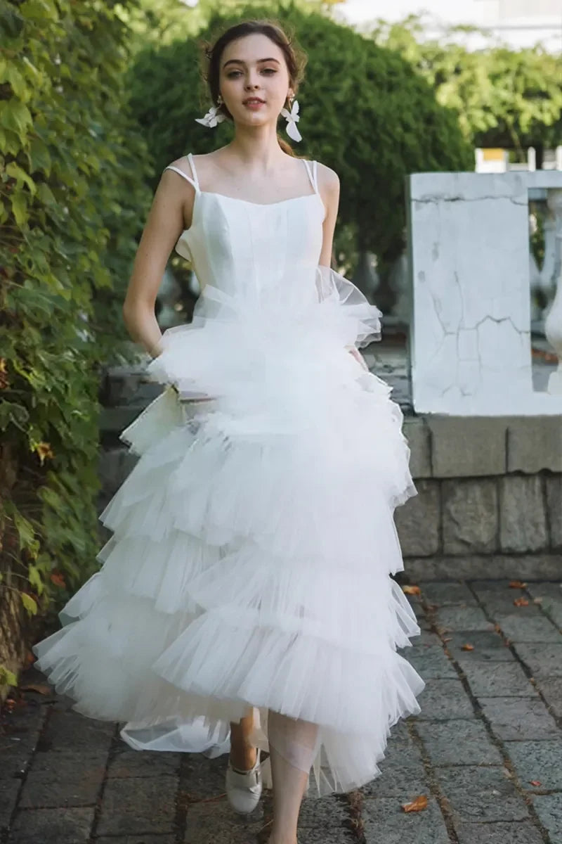 Mannequin en robe de mariée princesse bohème en tulle blanc multicouches lors d'un shooting, entouré de l'équipe créative de l'atelier — énergie libre et élégante
