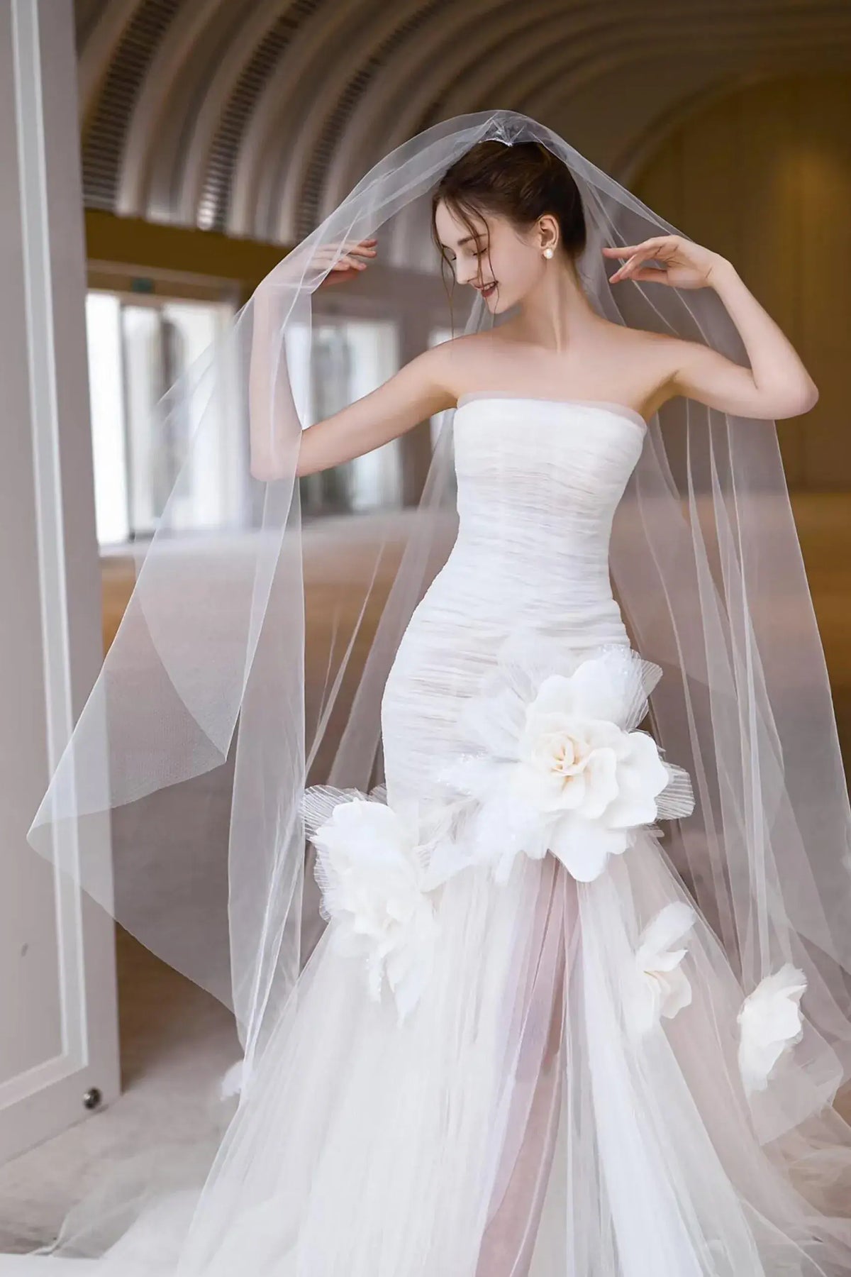 Mariée portant une robe sirène avec bustier et de spectaculaires fleurs 3D géantes en tulle.
