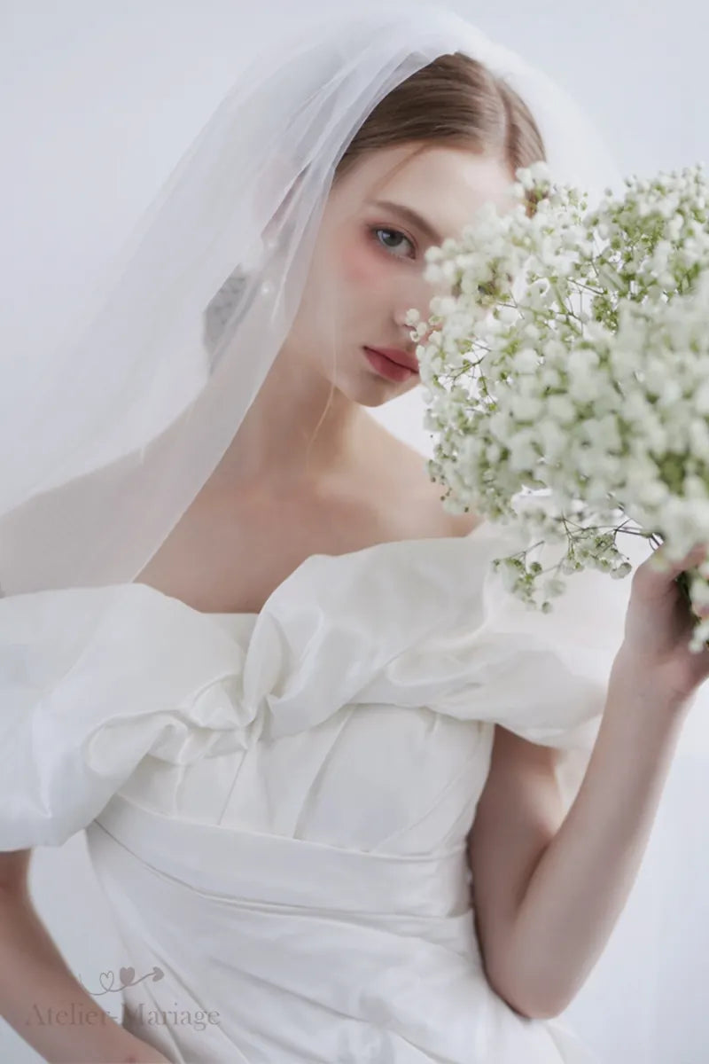 Mariée portant une robe en soie taffetas à épaules dénudées, tenant des fleurs