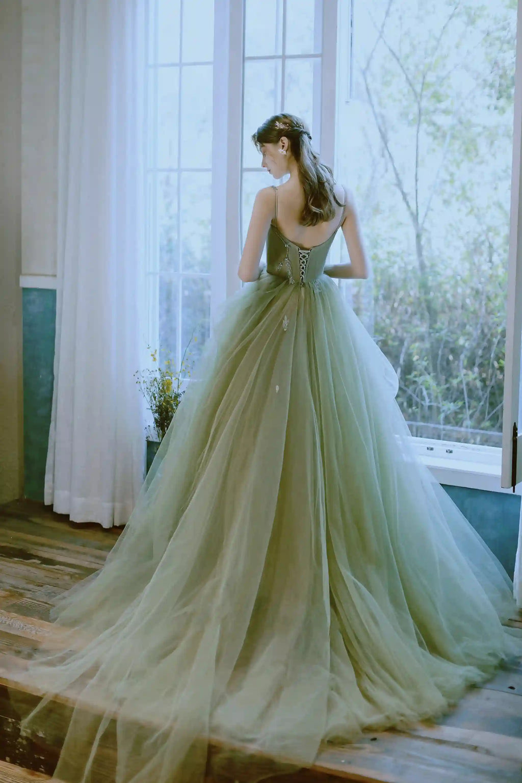 Mariée regardant par-dessus son épaule portant une robe féerique vert sauge avec fines bretelles.