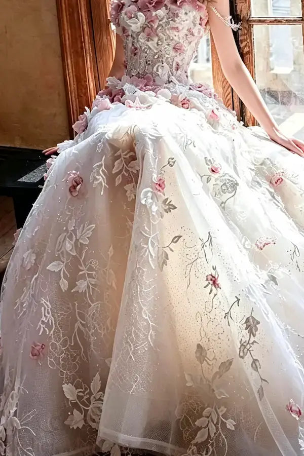 Vue rapprochée de la traîne féerique montrant le mélange de textures entre fleurs en relief et tulle haute gamme.