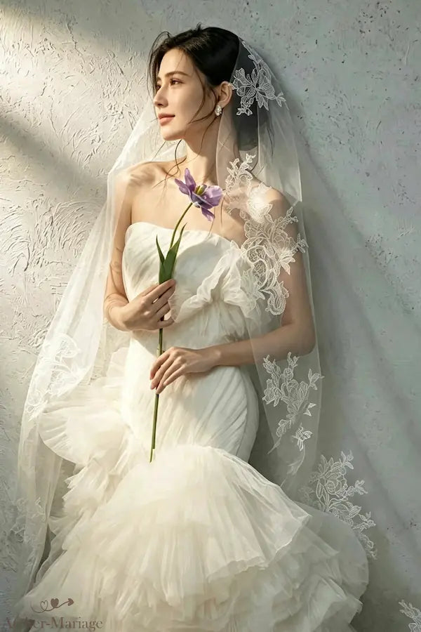 Profil élégant de la mariée en lumière naturelle, portant le voile en dentelle longue de 3m et tenant une tulipe mauve