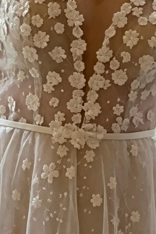 Zoom sur les finitions artisanales de la ceinture fine et des broderies de fleurs blanches sur une robe de mariée sur-mesure.