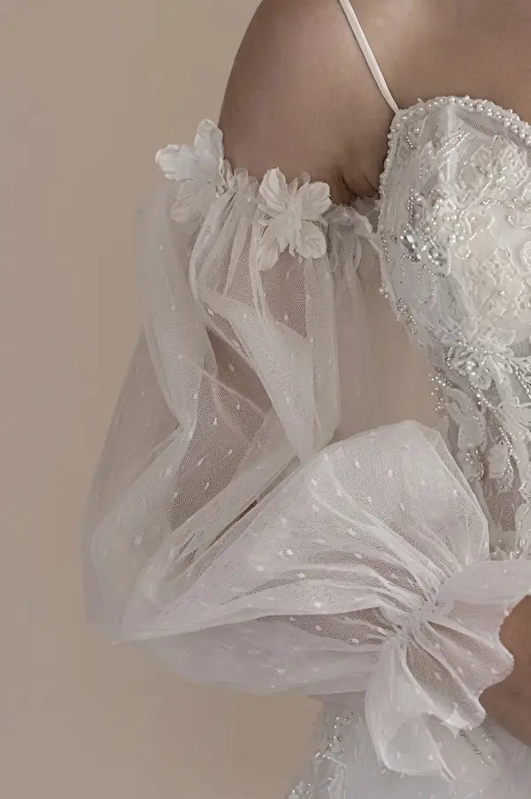 Zoom sur les applications de fleurs 3D sur le tulle extérieur vaporeux d'une manche de mariée.