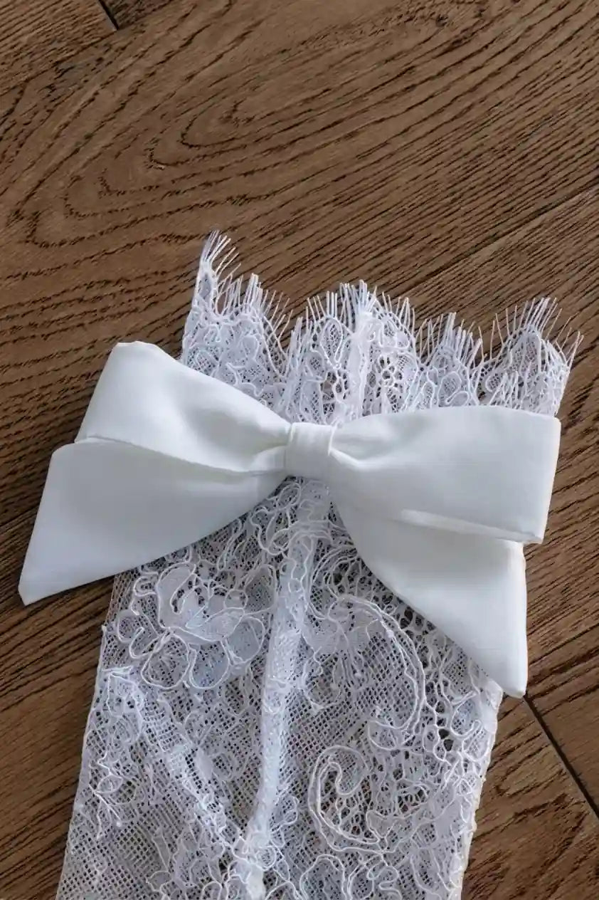 Vue rapprochée d'un nœud en satin soyeux cousu sur une manchette en dentelle artisanale.